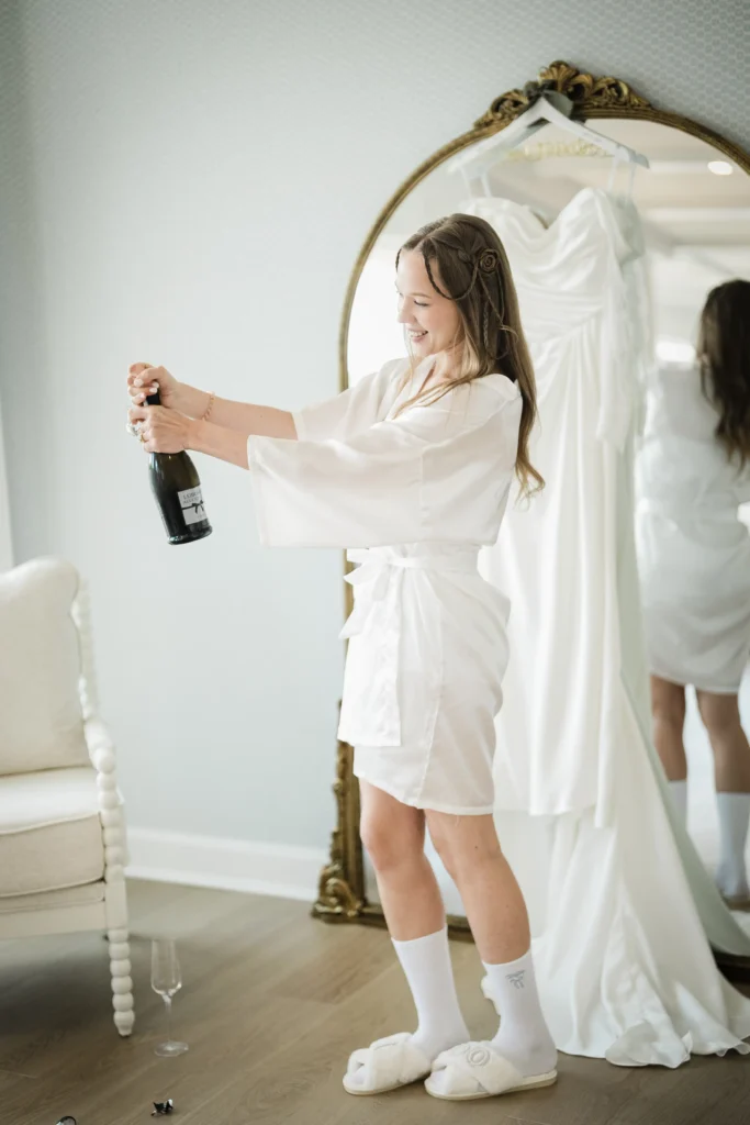 Bride opening champagne beside her wedding dress at The Mill Lakeside Manor