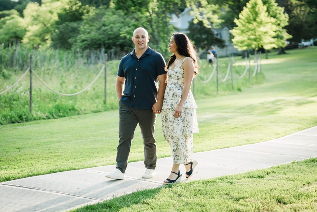 Engaged couple walking hand in hand past the meadow path at Burnham Park Morristown NJ