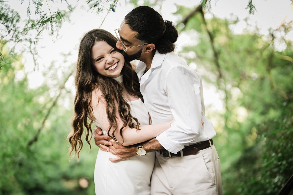 Candid save the date engagement photo of a couple laughing under garden trees