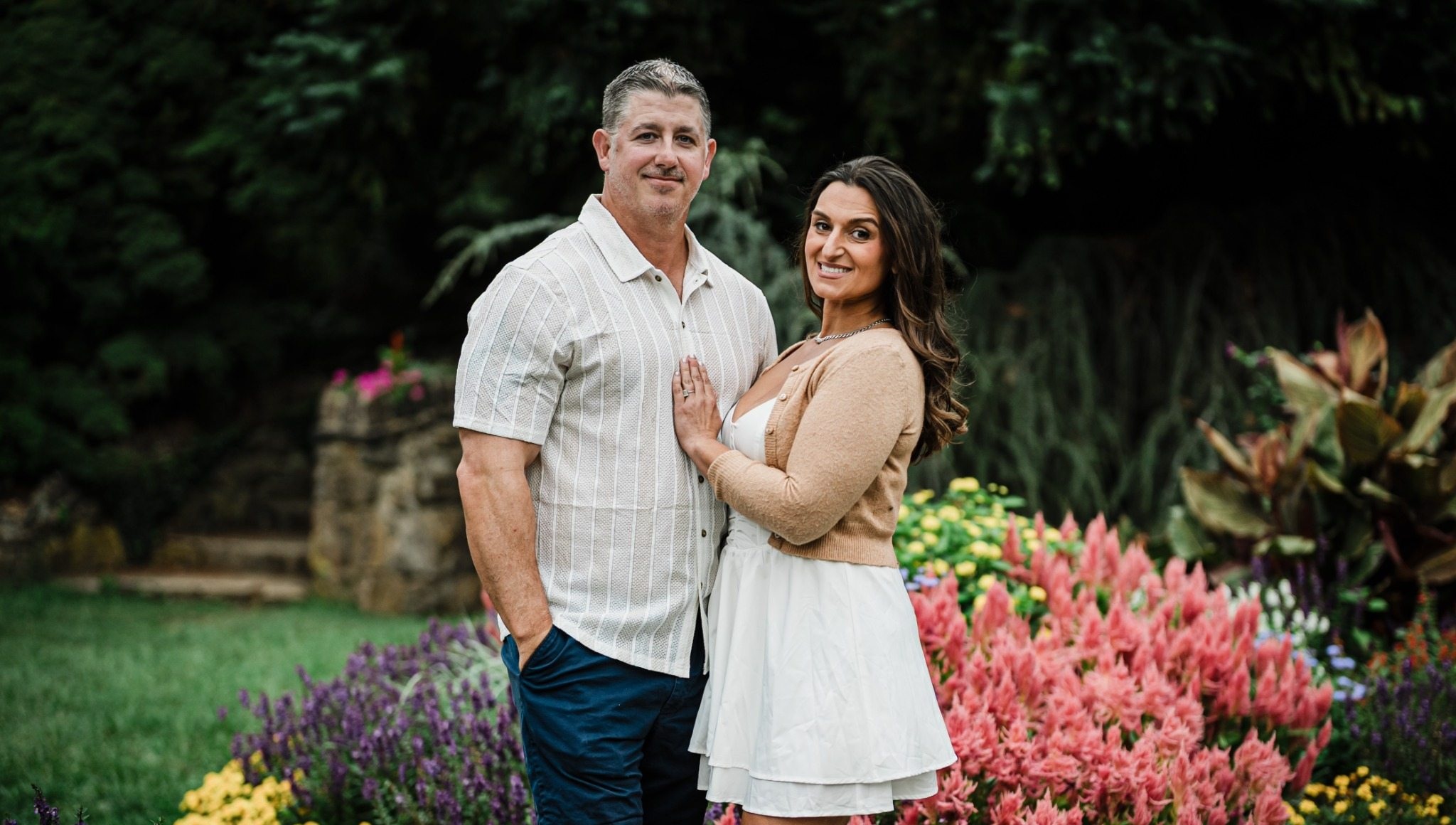 Engaged couple in relaxed neutral outfits embracing among colorful flowers at Deep Cut Gardens