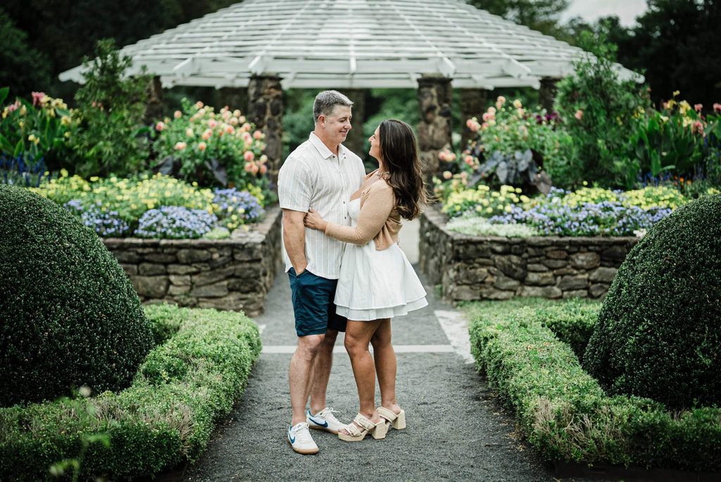 Couple embracing on a gravel path between clipped hedges and flower beds at Deep Cut Gardens