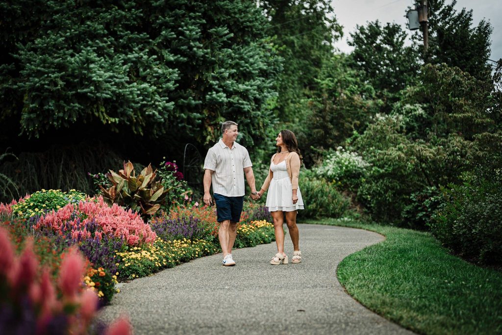 Engaged couple walking hand in hand along a curved garden path at Deep Cut Gardens
