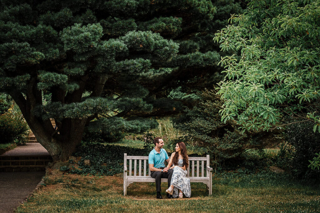 Engaged couple on a secluded bench under evergreens at Deep Cut Gardens in Middletown