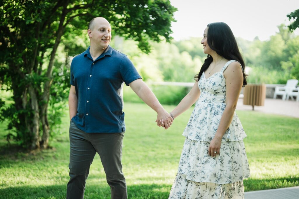 Engaged couple holding hands as they walk across the lawn at Burnham Park in Morristown