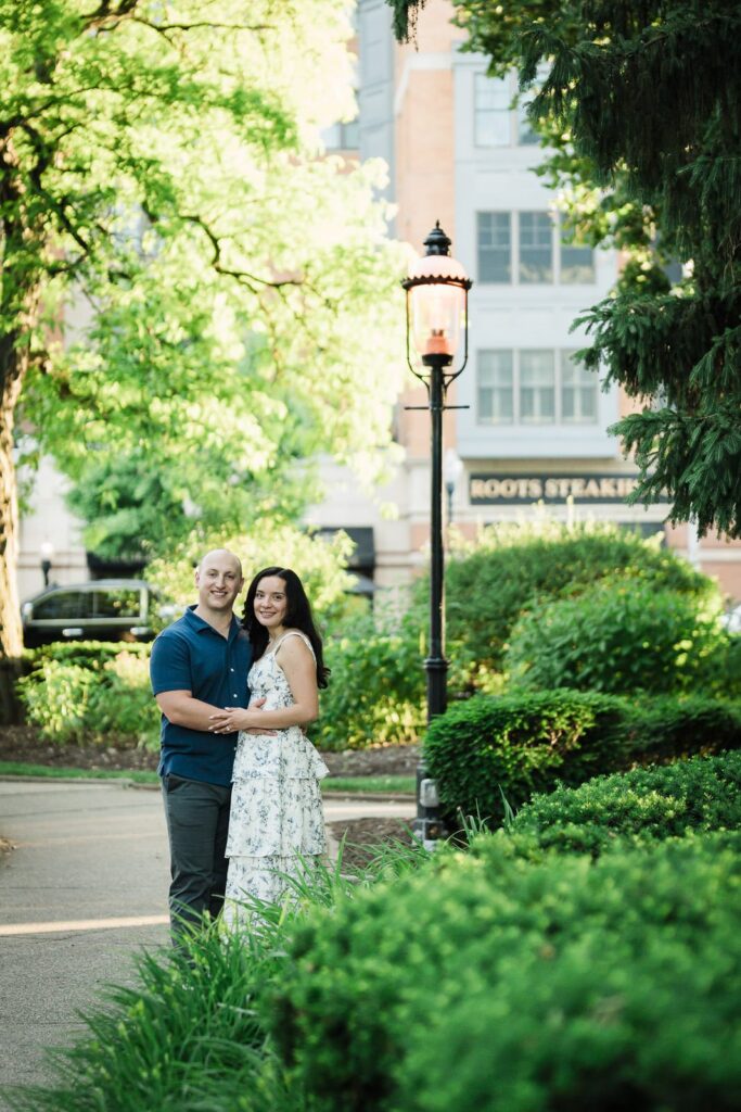 Engaged couple standing beside a gas lamp on a downtown Morristown sidewalk at golden hour