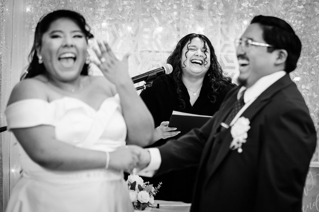 Officiant laughing with the bride and groom during their vows in black and white