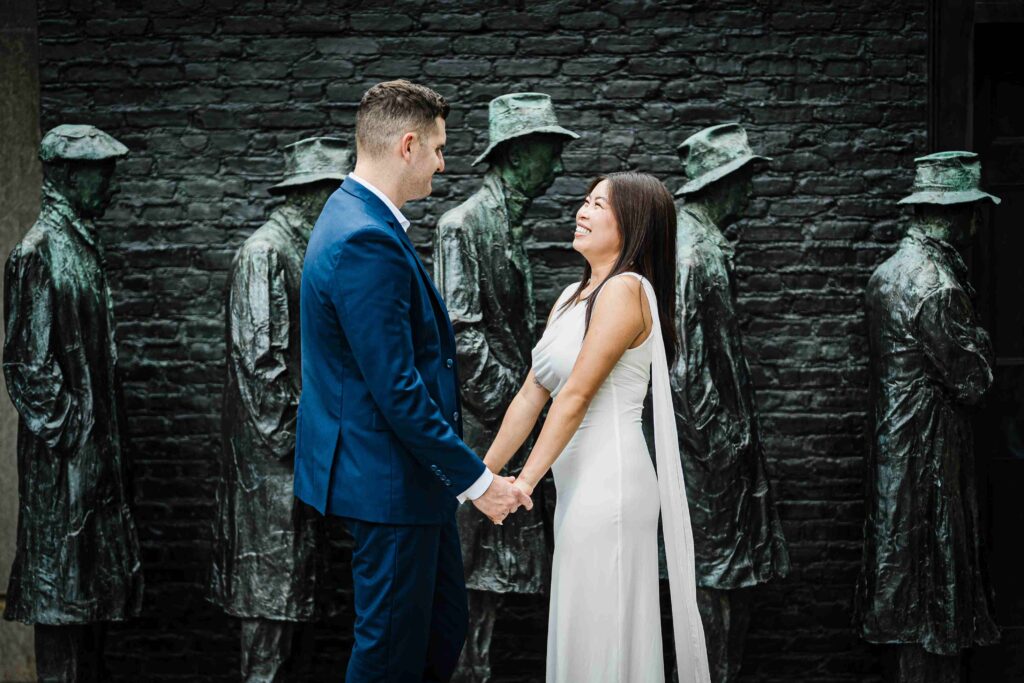 Engaged couple holding hands and laughing beside bronze sculpture figures at Grounds For Sculpture NJ