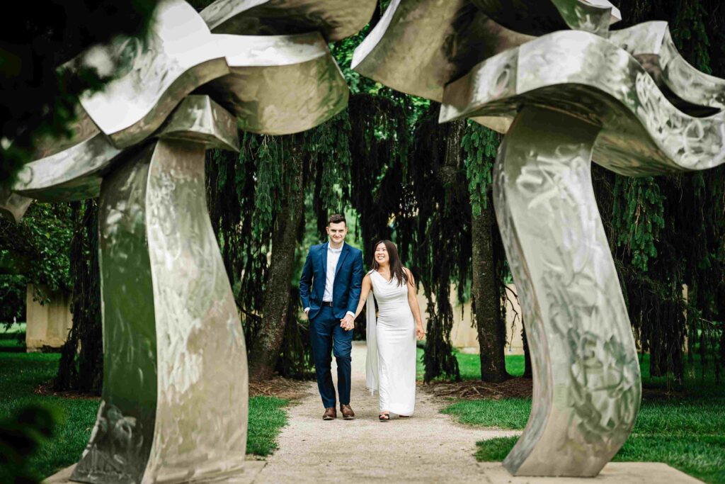 Couple walking hand in hand beneath a stainless steel sculpture arch at Grounds For Sculpture NJ