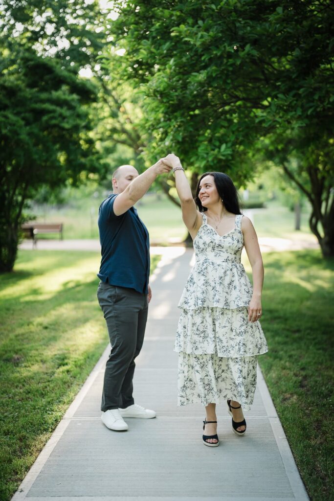 Engaged couple dancing and spinning on a tree lined path at Burnham Park Morristown NJ