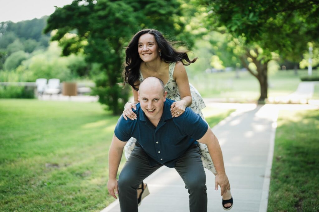 Man giving his fiancee a piggyback ride on the path at Burnham Park Morristown NJ