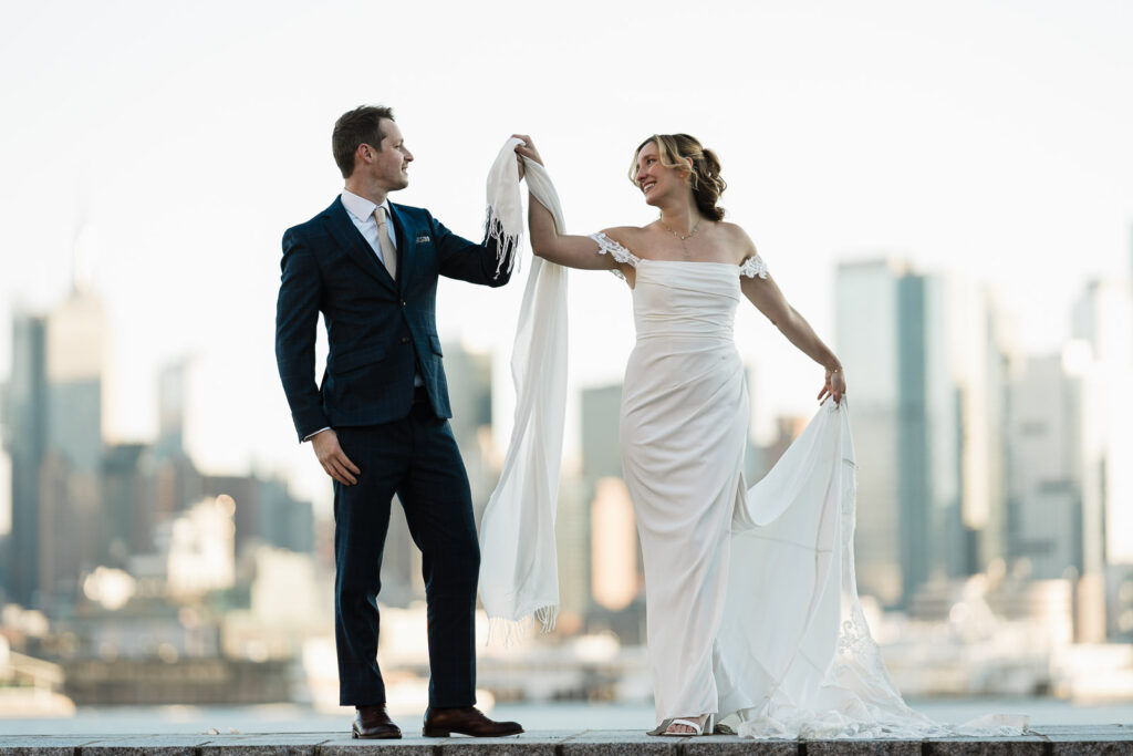 Bride twirling beside groom during waterfront wedding portraits with skyline behind them