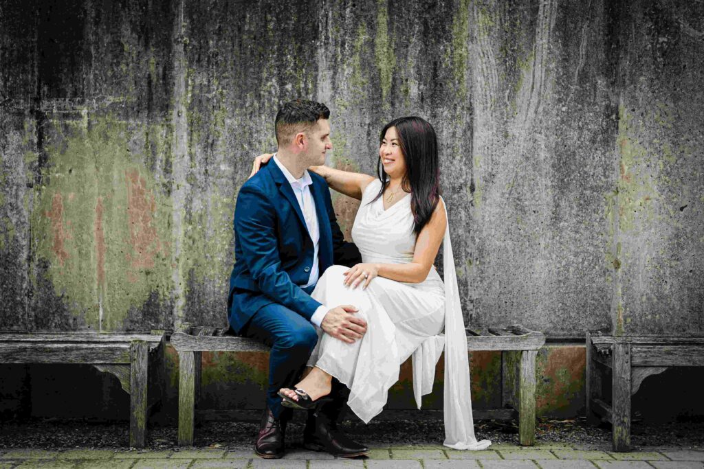 Yia and Jeremiah seated on a wooden bench against a concrete wall at Grounds For Sculpture