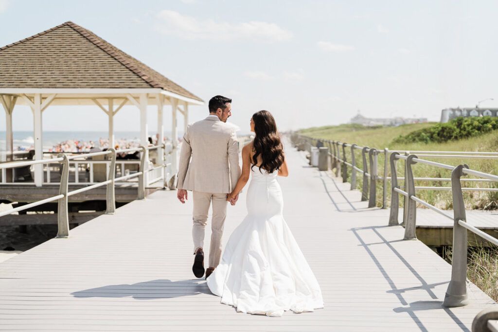 Bride and groom walking a Jersey Shore boardwalk in bright midday sunlight