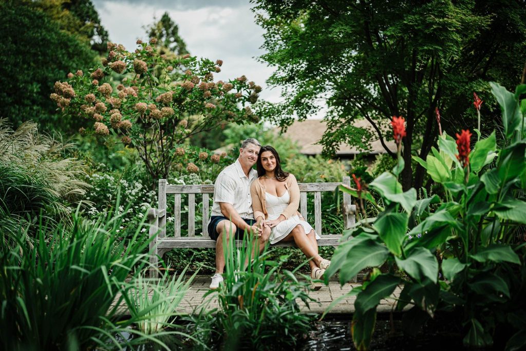 Engaged couple sitting close together on a garden bench at Deep Cut Gardens