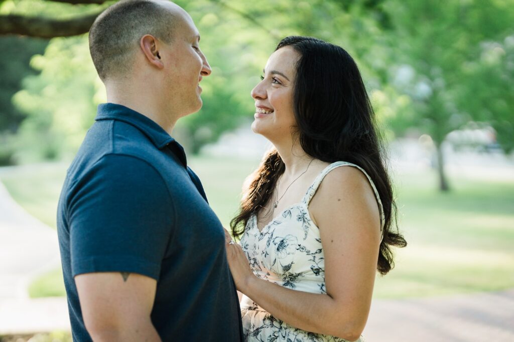 Engaged couple looking at each other and laughing under the trees at Burnham Park Morristown