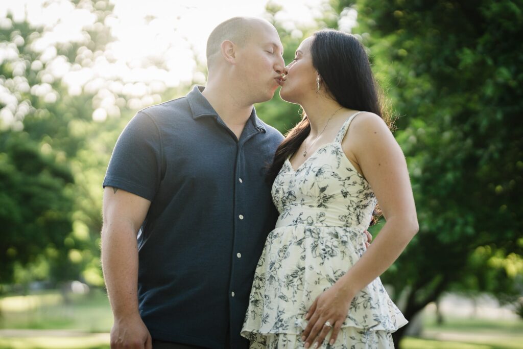 Engaged couple kissing in golden evening light under the trees at Burnham Park Morristown