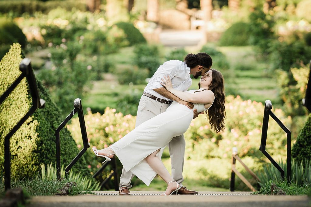 Couple dancing and dipping during save the date engagement photos in a garden