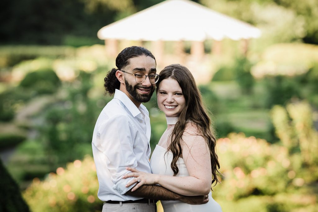 Couple embracing for save the date engagement photos in front of a garden gazebo