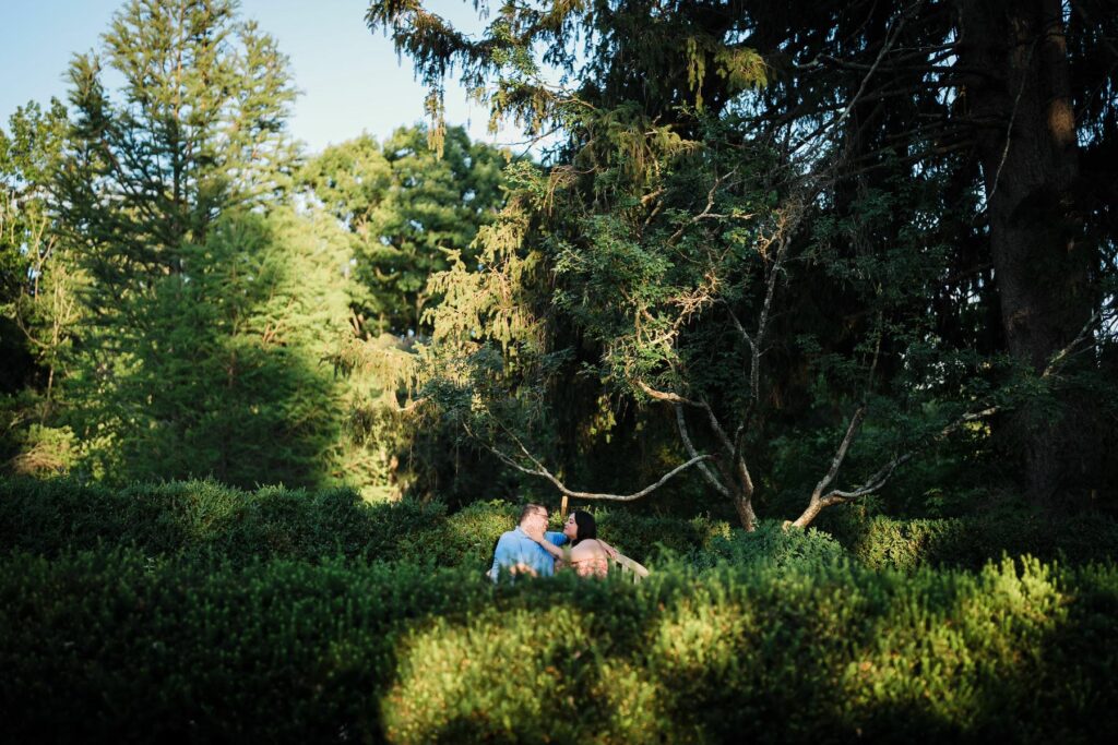 Engaged couple sitting together in summer greenery during a New Jersey session