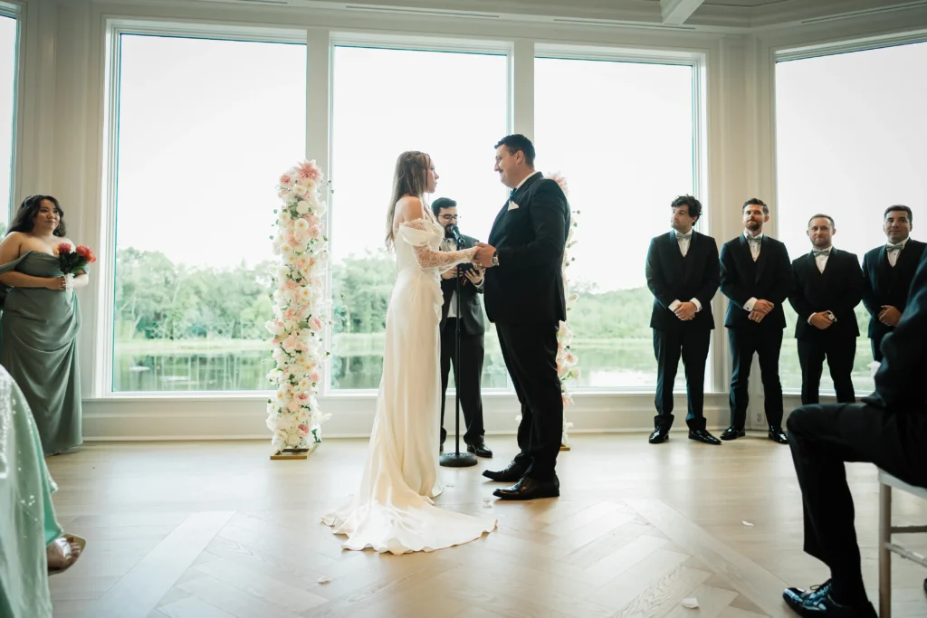 Bride and groom exchanging vows before the lake windows at The Mill Lakeside Manor
