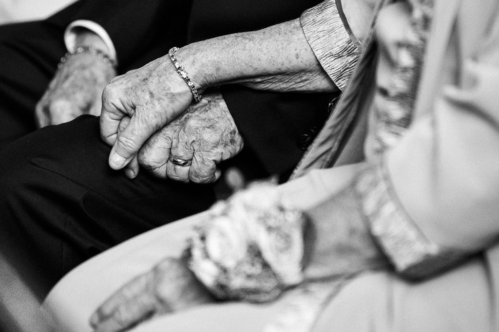 Grandparents holding hands during a wedding ceremony in a black and white detail photo