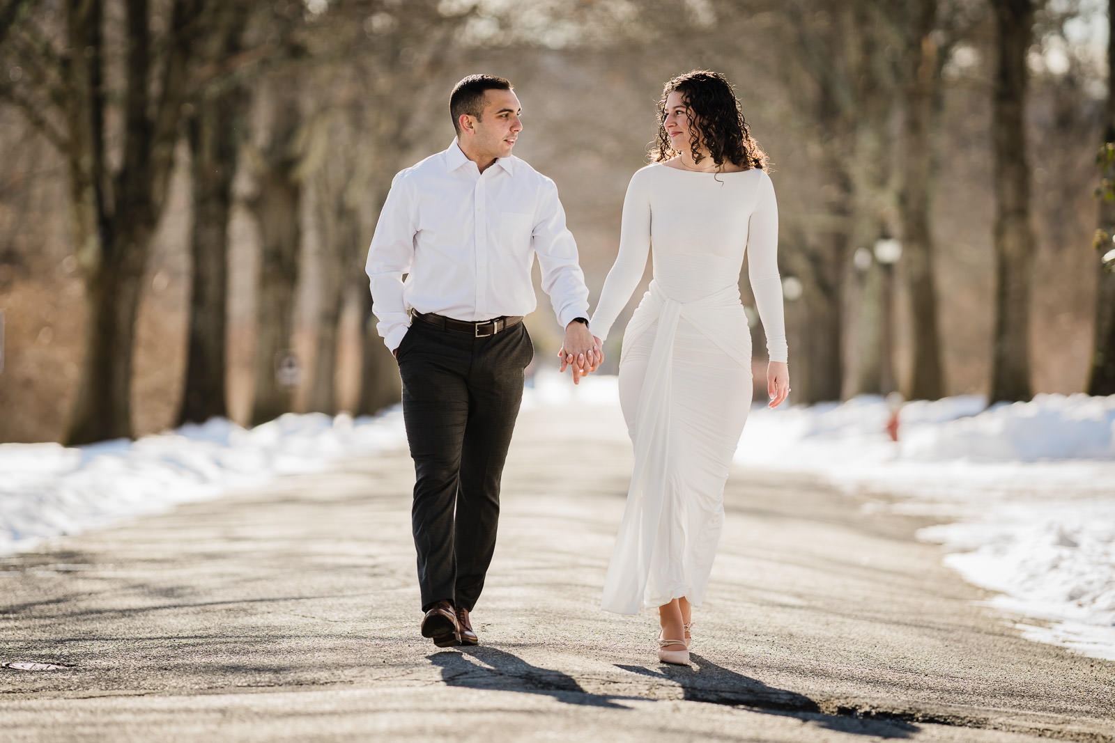 Engaged couple walking hand in hand down a snow-lined path at Skylands in Ringwood NJ