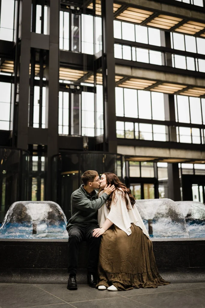 Couple kissing on a fountain ledge beneath Bell Works glass and steel architecture