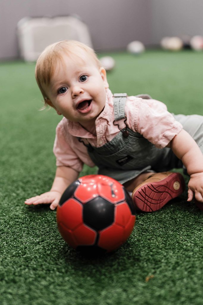 Smiling toddler crawling across indoor turf during a birthday party in Manhattan