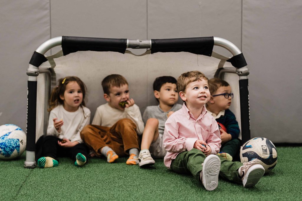 Young party guests sitting together inside a mini soccer goal at Crossbar NYC