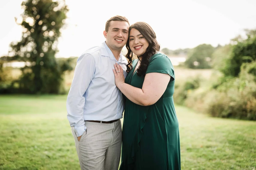 Engaged couple smiling cheek to cheek on the lawn at Harkness Memorial State Park