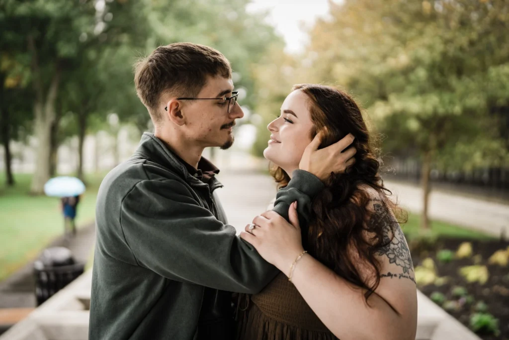 Engaged couple face to face on a wet walkway with umbrella in background