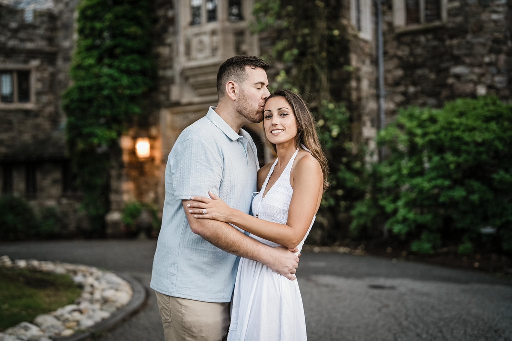 Jonathan and Emma embracing in front of the stone manor at Skylands Manor in New Jersey
