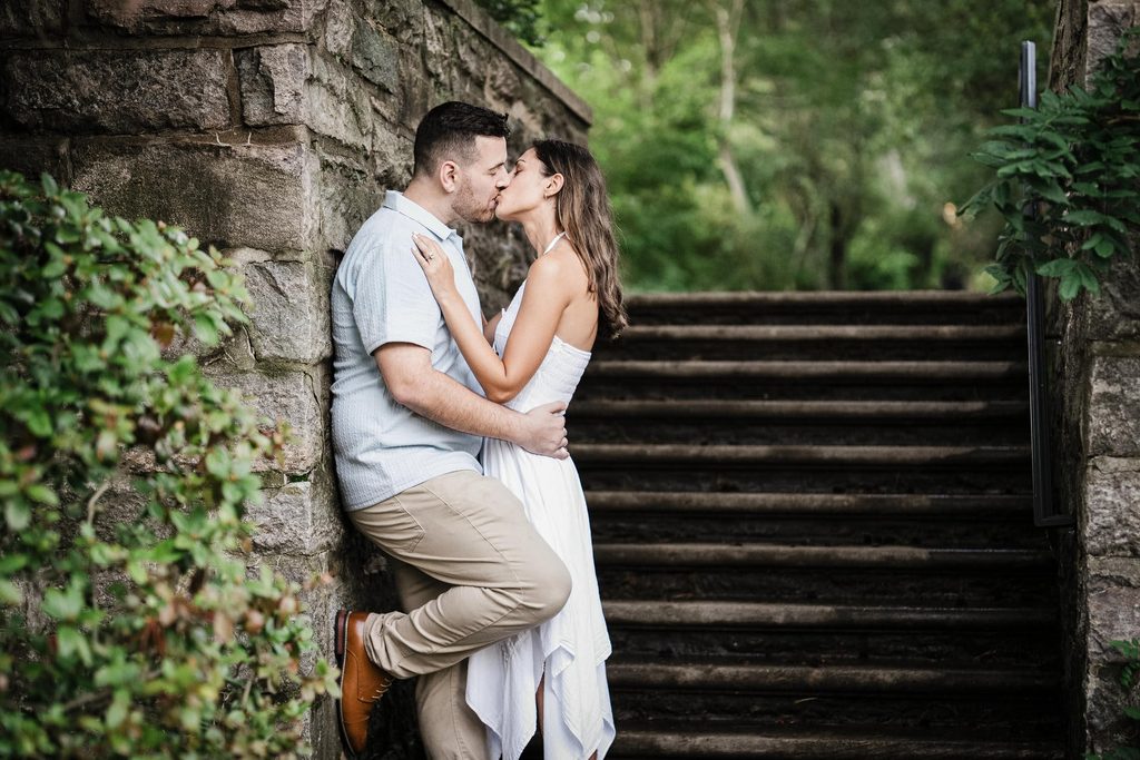 Jonathan and Emma kissing against a stone staircase wall at Skylands Manor