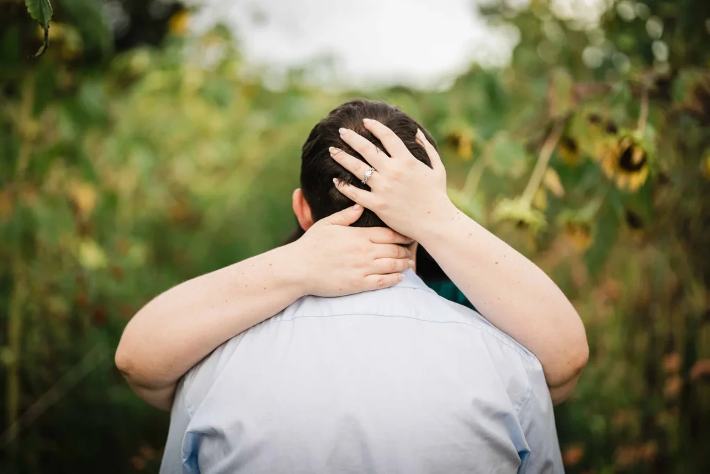 Engagement ring visible as a woman embraces her partner among sunflowers at Harkness