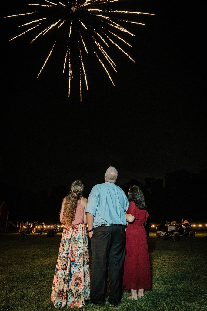 Bride and groom standing together as fireworks light the sky in Franklin Township