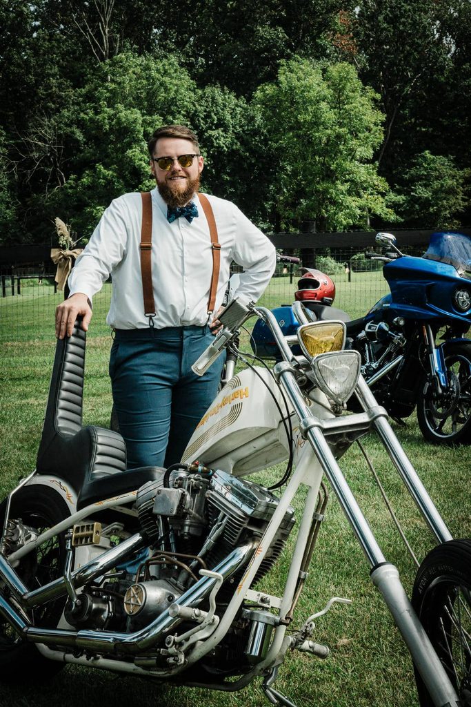 Man in suspenders standing beside a chopper motorcycle at a Franklin Township backyard wedding