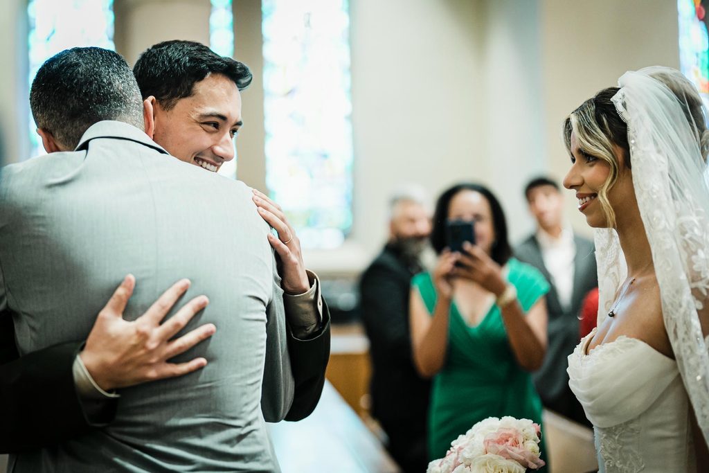 Groom hugging the bride's escort at the altar during a Harrison NY church wedding