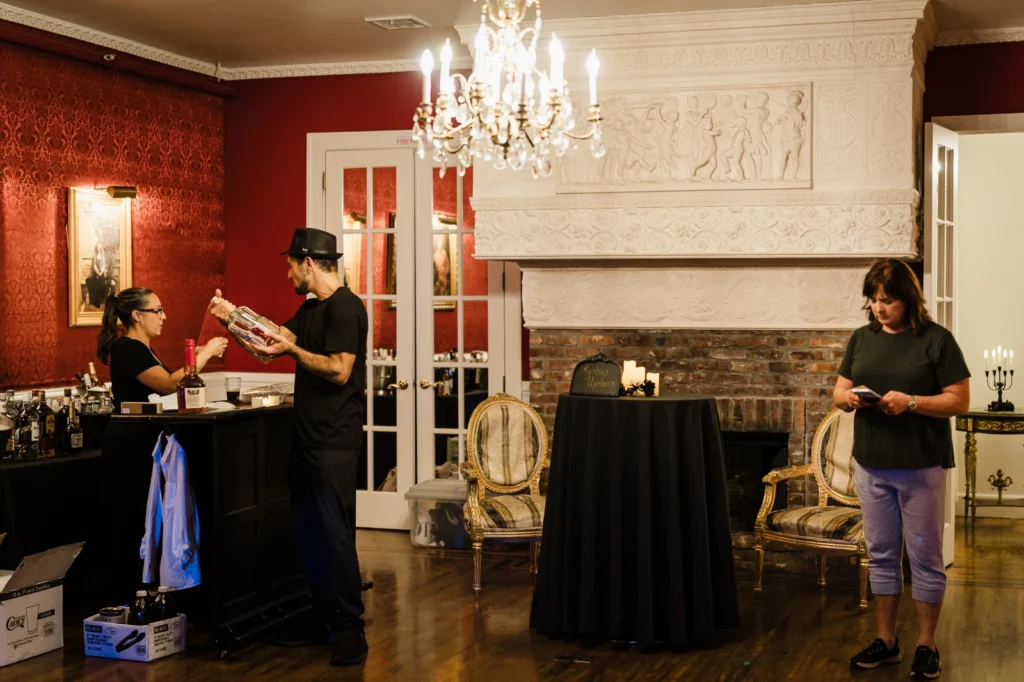 Staff preparing the bar beneath a chandelier and carved mantel at James Ward Mansion