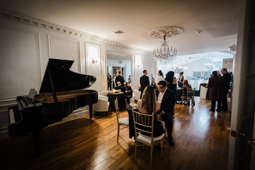 Masked guests talking at small tables beside a grand piano at James Ward Mansion in Westfield