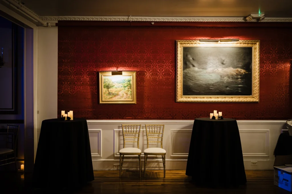 Gilt-framed paintings above candlelit tables in a red damask room at James Ward Mansion