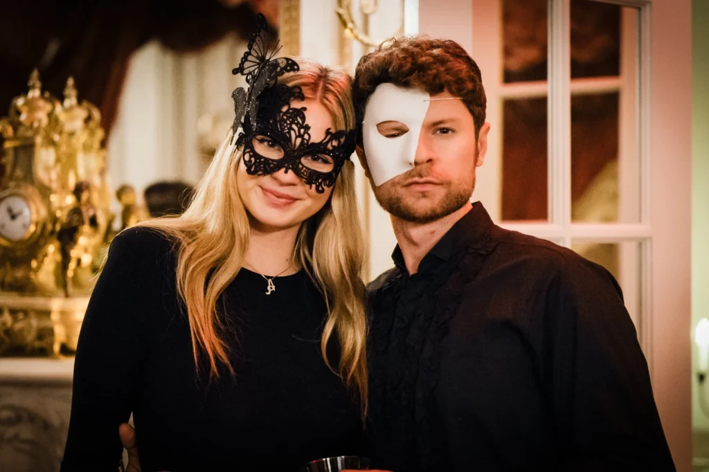 Two masked guests in black leaning together for a portrait at James Ward Mansion