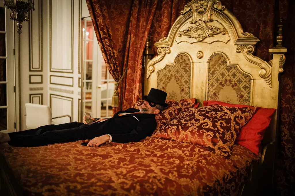 Masked guest in a top hat reclining on a gilded bed at James Ward Mansion