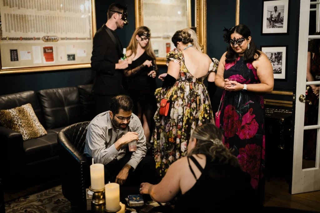 Masked guests gather around a tarot reading in a teal lounge at James Ward Mansion