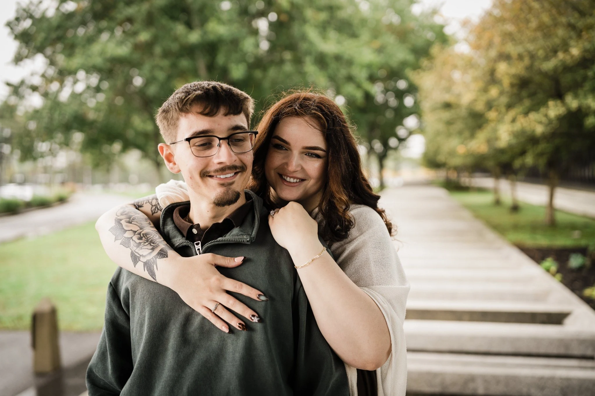 Smiling couple embracing on a tree-lined walkway near Bell Works in Holmdel