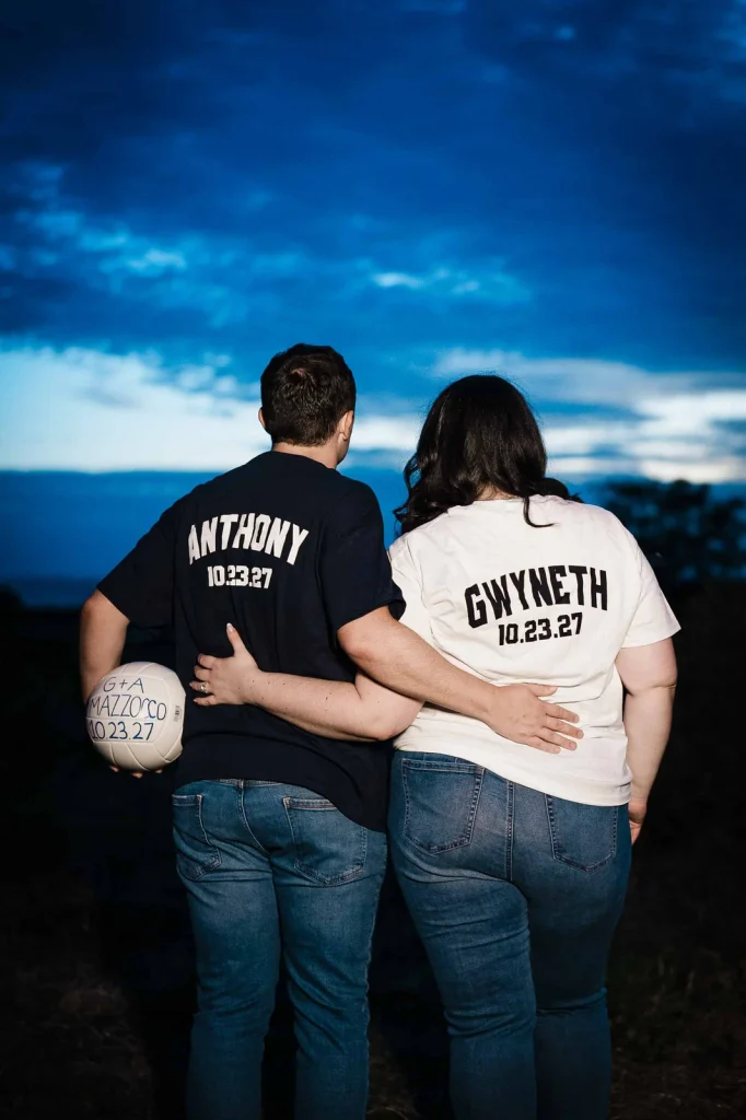 Engaged couple in personalized shirts looking toward the evening sky at Harkness