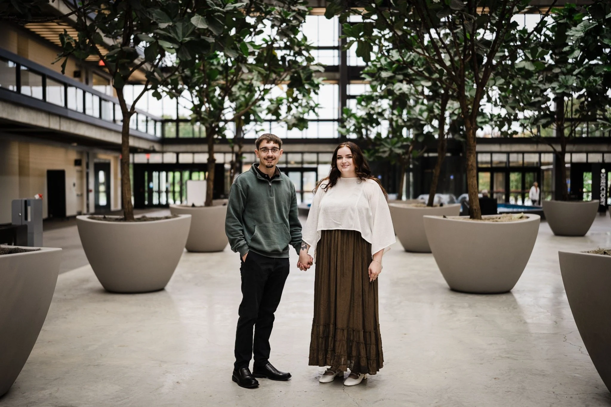 Samuel and Savannah holding hands among indoor trees at Bell Works in Holmdel