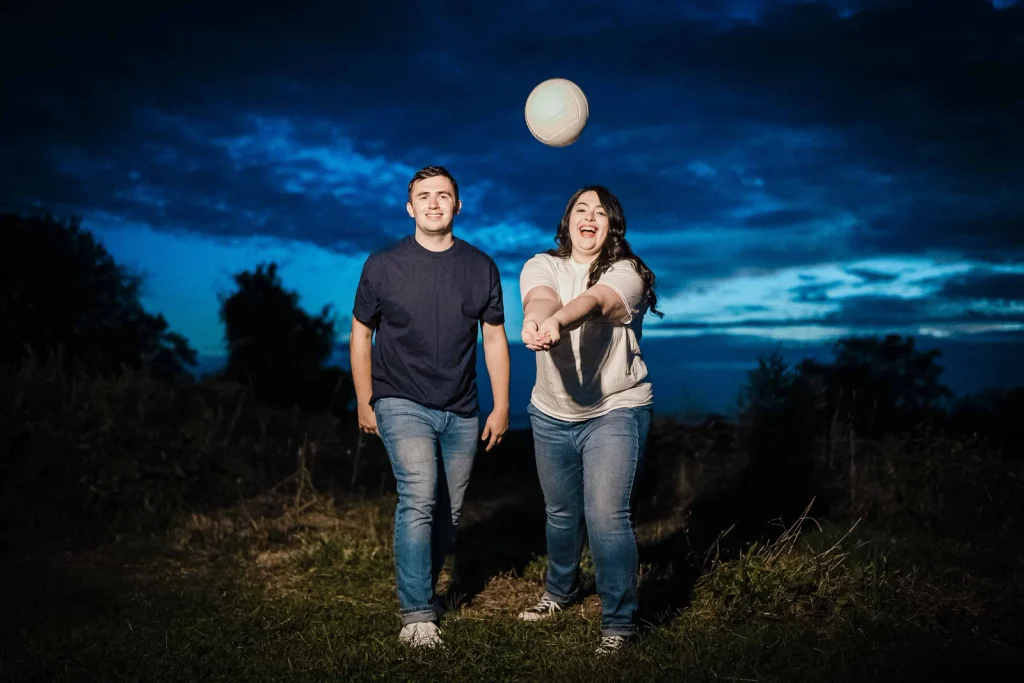 Couple tossing a volleyball at dusk during a Harkness Memorial State Park engagement session